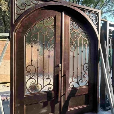 Premium Cast Iron Spiral Staircases by Like Metal are displayed outdoors in sunlight, with spiral designs casting shadows. In the background, trees and a wooden fence enhance the scene.