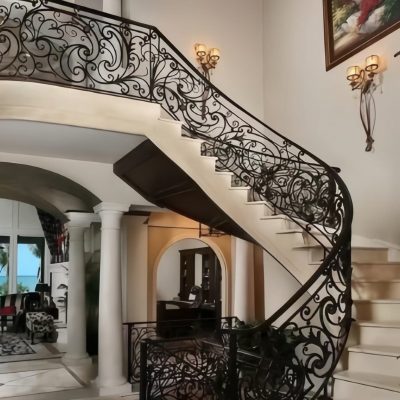 The Premium Cast Iron Spiral Staircases by Like Metal feature ornate black railings, marble floors, arched entries, columns, elegant lighting, and large windows that offer scenic outdoor views for a luxurious home interior.