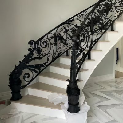 Premium Cast Iron Spiral Staircases by Like Metal feature ornate black floral railings. The white staircase sits on gray-veined marble flooring, with protective white sheets covering the stair base.