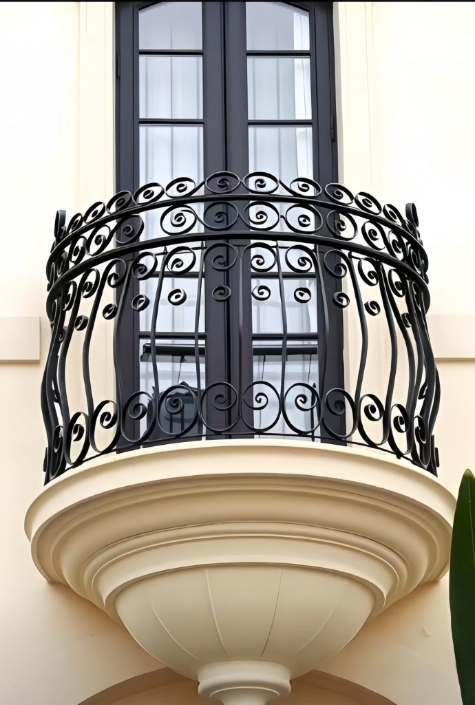 A Premium Cast Iron Spiral Staircase by Like Metal adorns a cream-colored building, positioned near tall arched double doors with glass panels and a green plant visible on the right side.