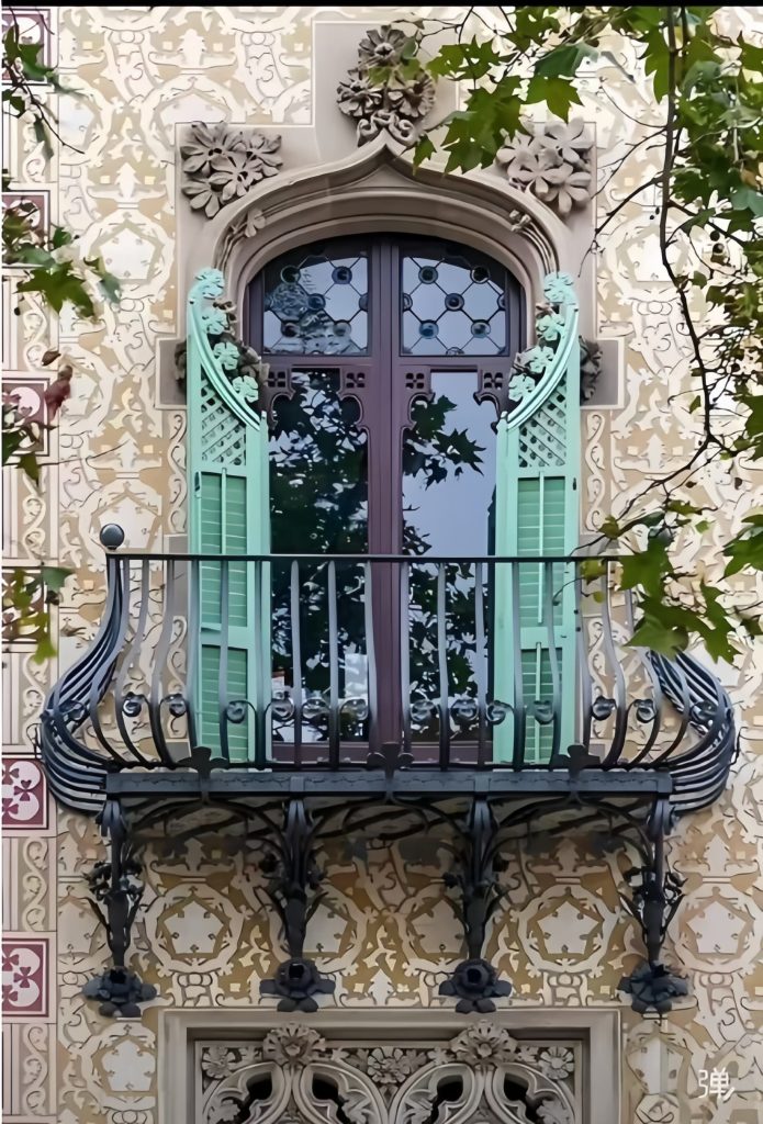 A decorative balcony with Premium Cast Iron Spiral Staircases by Like Metal, mint green shutters, and an arched window, set in a beige facade with floral designs and leafy branches partially visible.