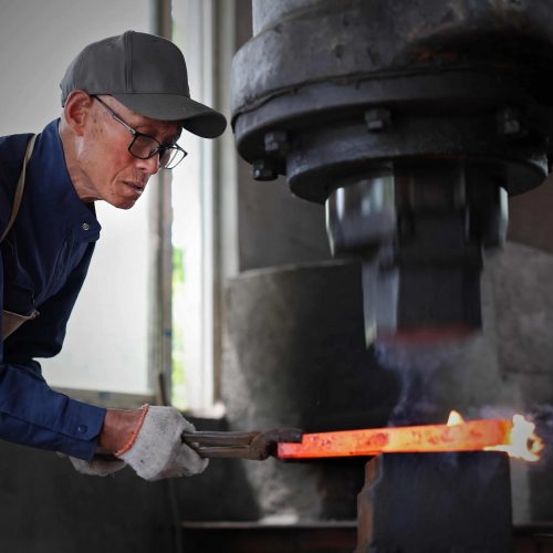 LIKE Metal wrought iron gate forging process showing red-hot steel bars being hammered and shaped on an anvil by skilled blacksmiths, with close-up views of decorative scroll bending, twisting, and flattening techniques, demonstrating traditional ironworking artistry combined with precision fabrication for custom entry gates, balcony railings, and staircase components.